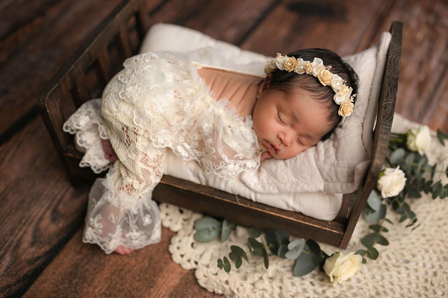 Newborn baby swaddled in white wrap with green cloth, surrounded by red roses and gold star halo decoration.