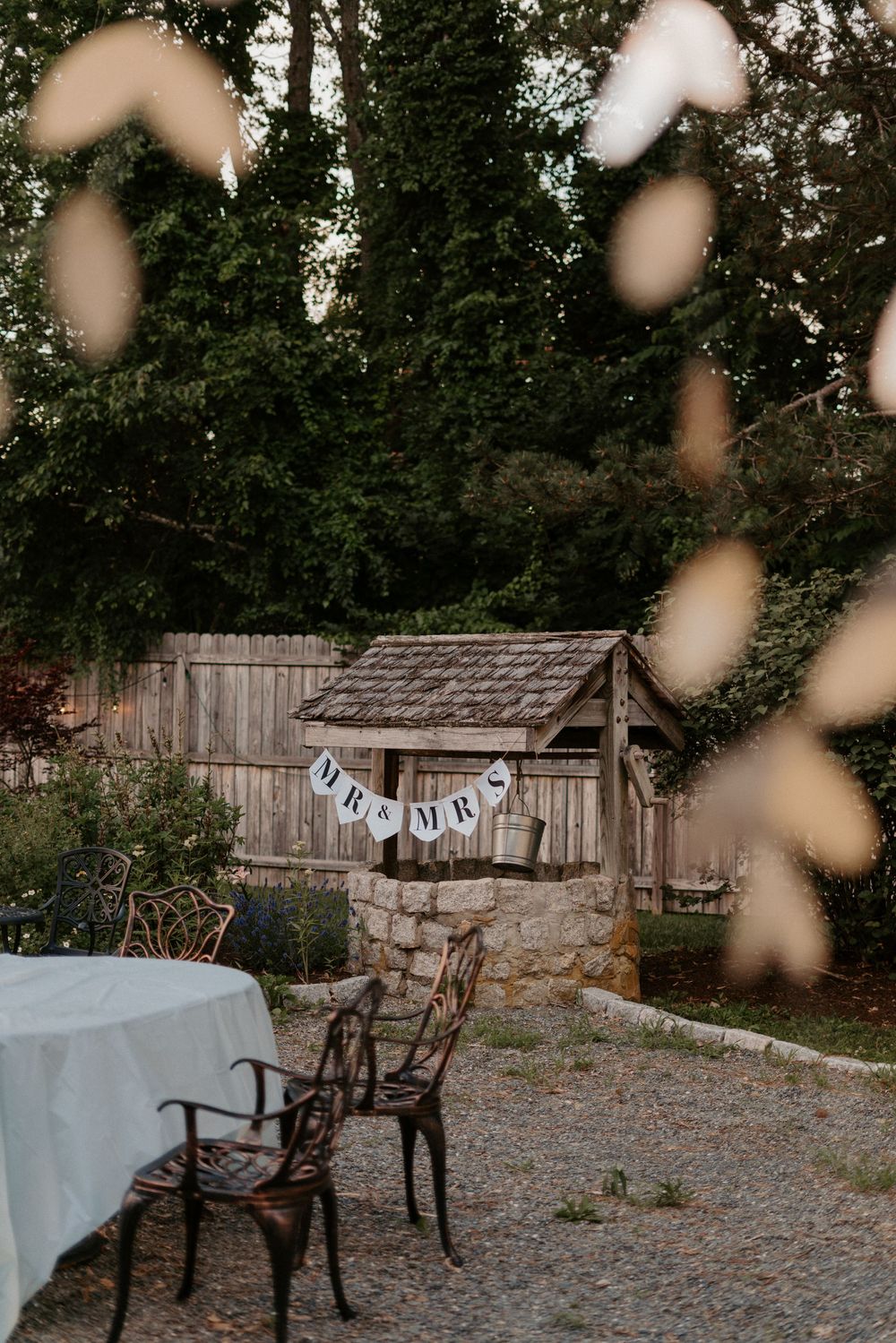 Rustic outdoor wedding venue with wooden wishing well decorated with Mr & Mrs banner and vintage chairs.