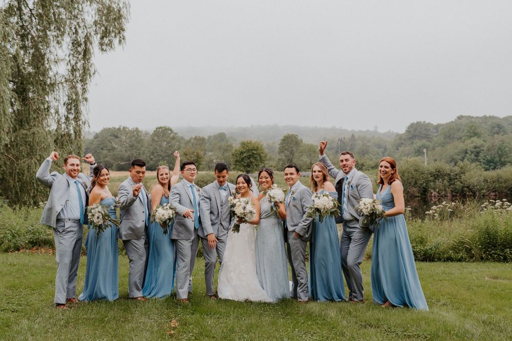Wedding party in blue dresses and gray suits celebrating outdoors on a cloudy day.