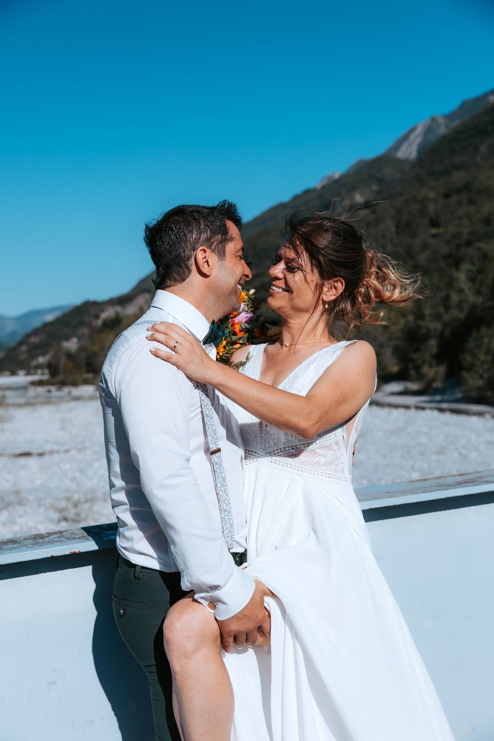 Bride and groom embrace on a snowy mountain backdrop under a clear blue sky on their winter wedding day.