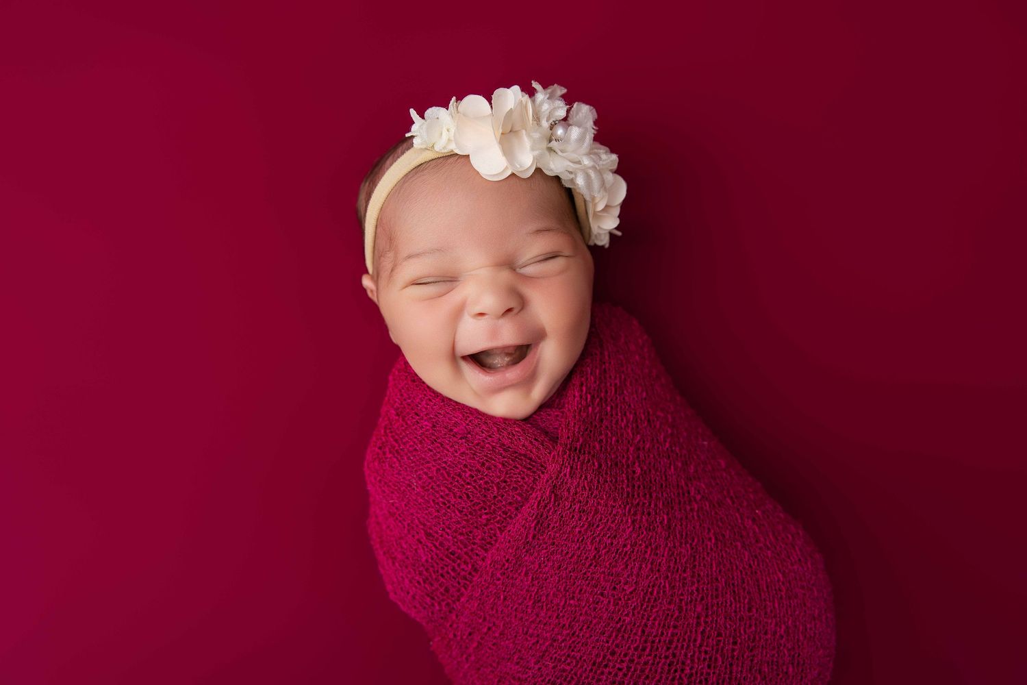 Happy South Asian family of four posing for a studio portrait with newborn baby wrapped in white cloth.