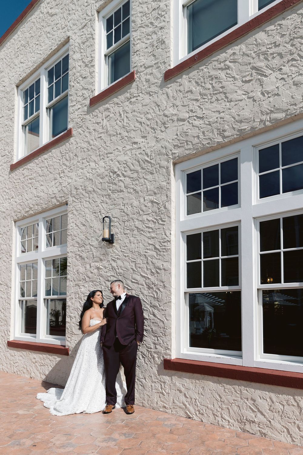 Bride and groom posing together outside elegant white stone wedding venue on sunny day.