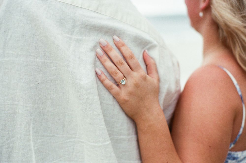 Close-up of a woman's hand with an engagement ring resting on a man's white linen shirt.