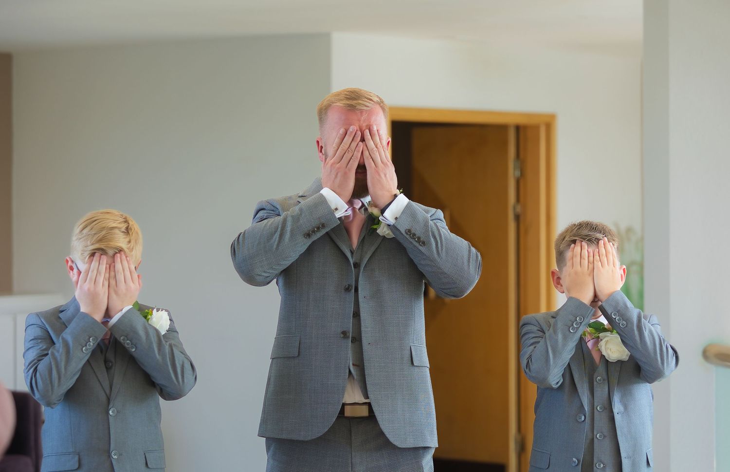 Three men in gray suits covering their faces with hands at a wedding ceremony.