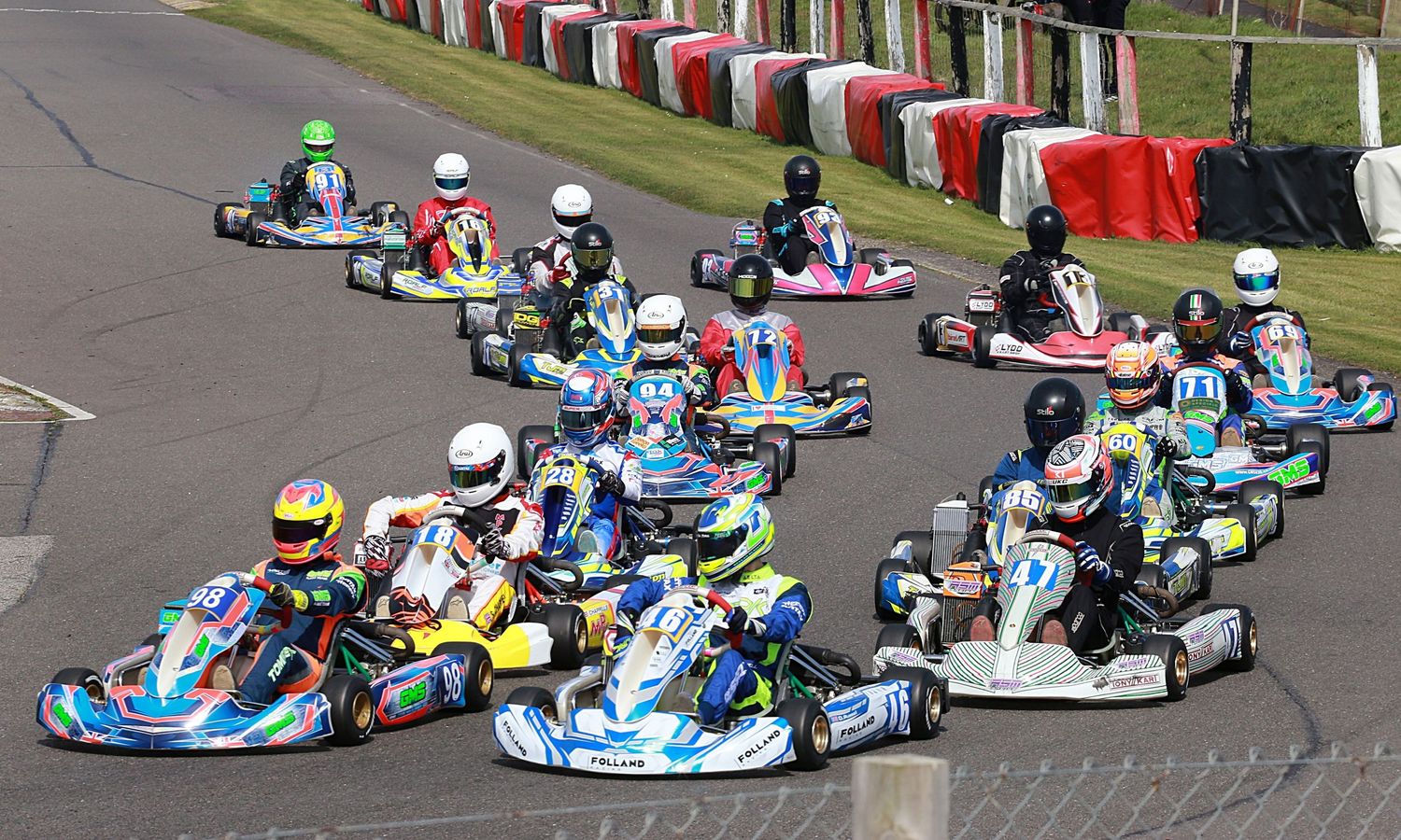 Large group of colorful go-karts racing together on a circuit track.