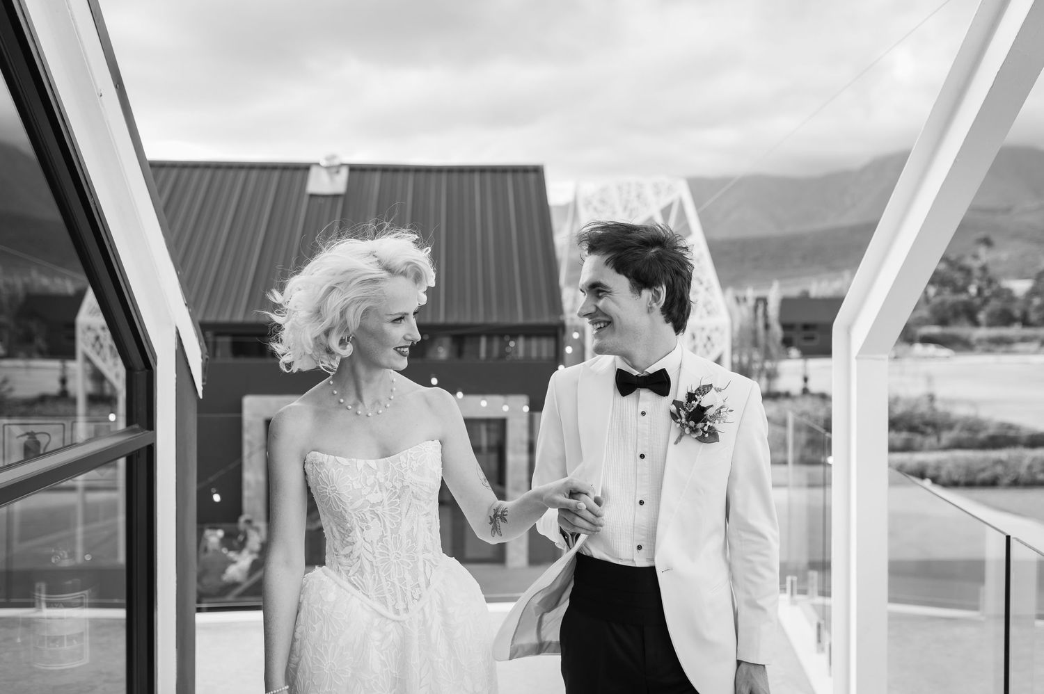 Bride and groom holding hands smiling at each other on a balcony in black and white wedding photo.