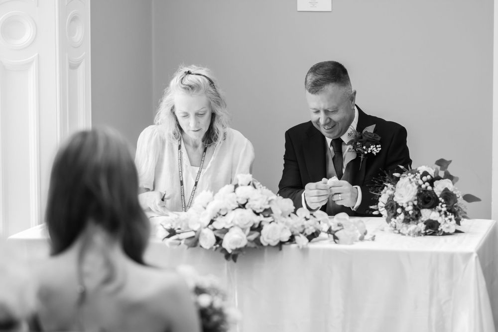 Black and white wedding photo of couple signing marriage register at decorated table with floral arrangements.
