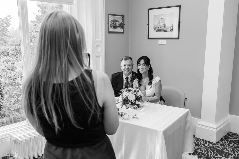 Photographer capturing a couple seated at a decorated table during a wedding ceremony in an elegant room.