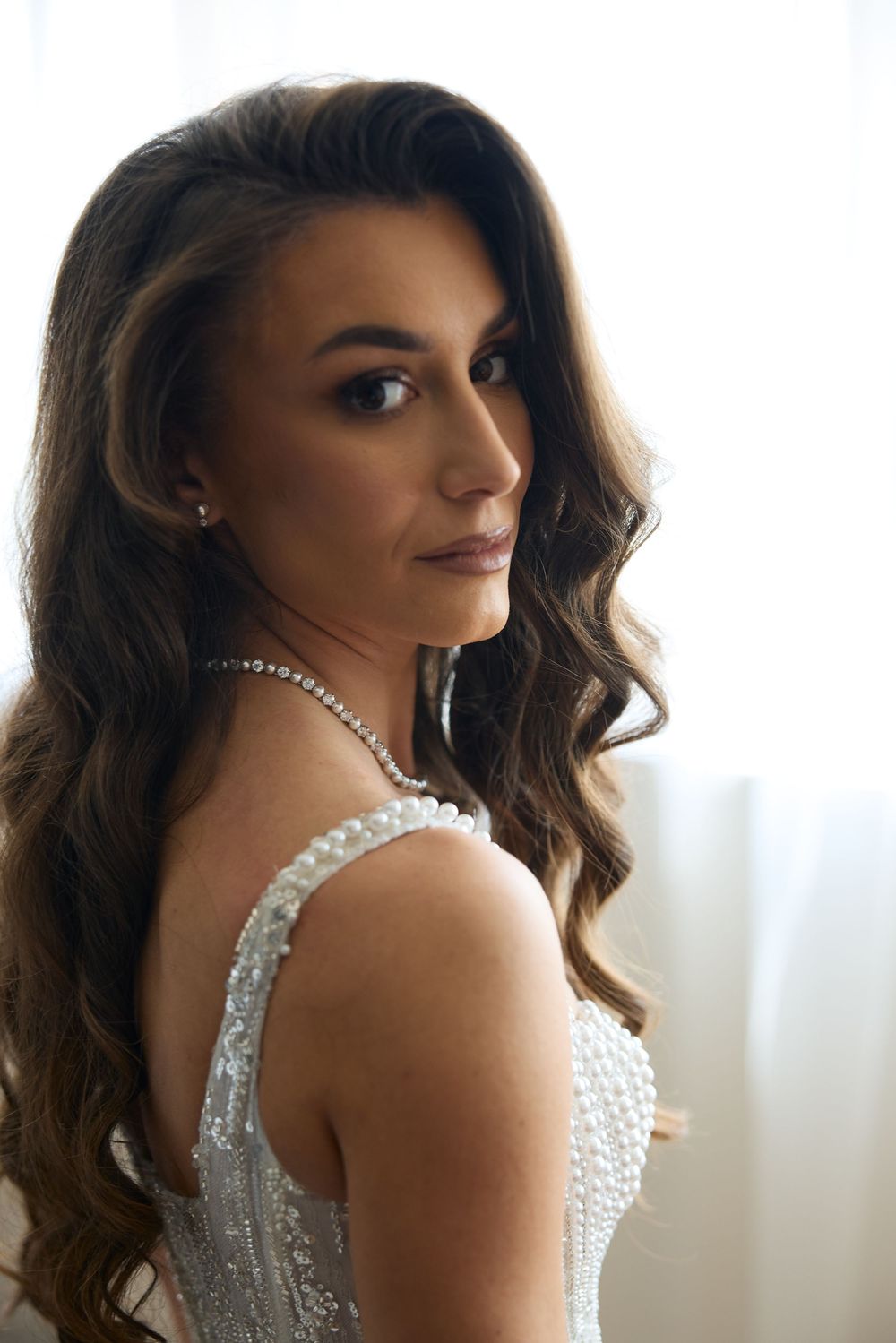Close-up portrait of a brunette bride wearing a pearl necklace and elegant sequined wedding dress.