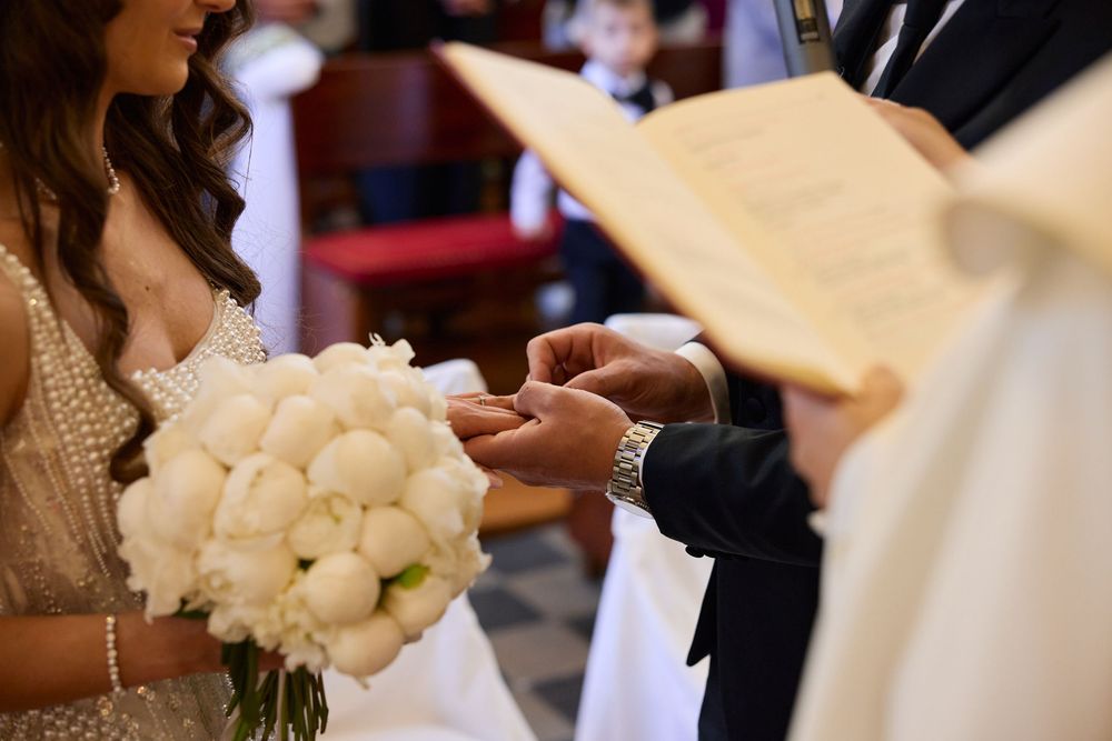 Close-up of groom placing wedding ring on brides finger during church ceremony.
