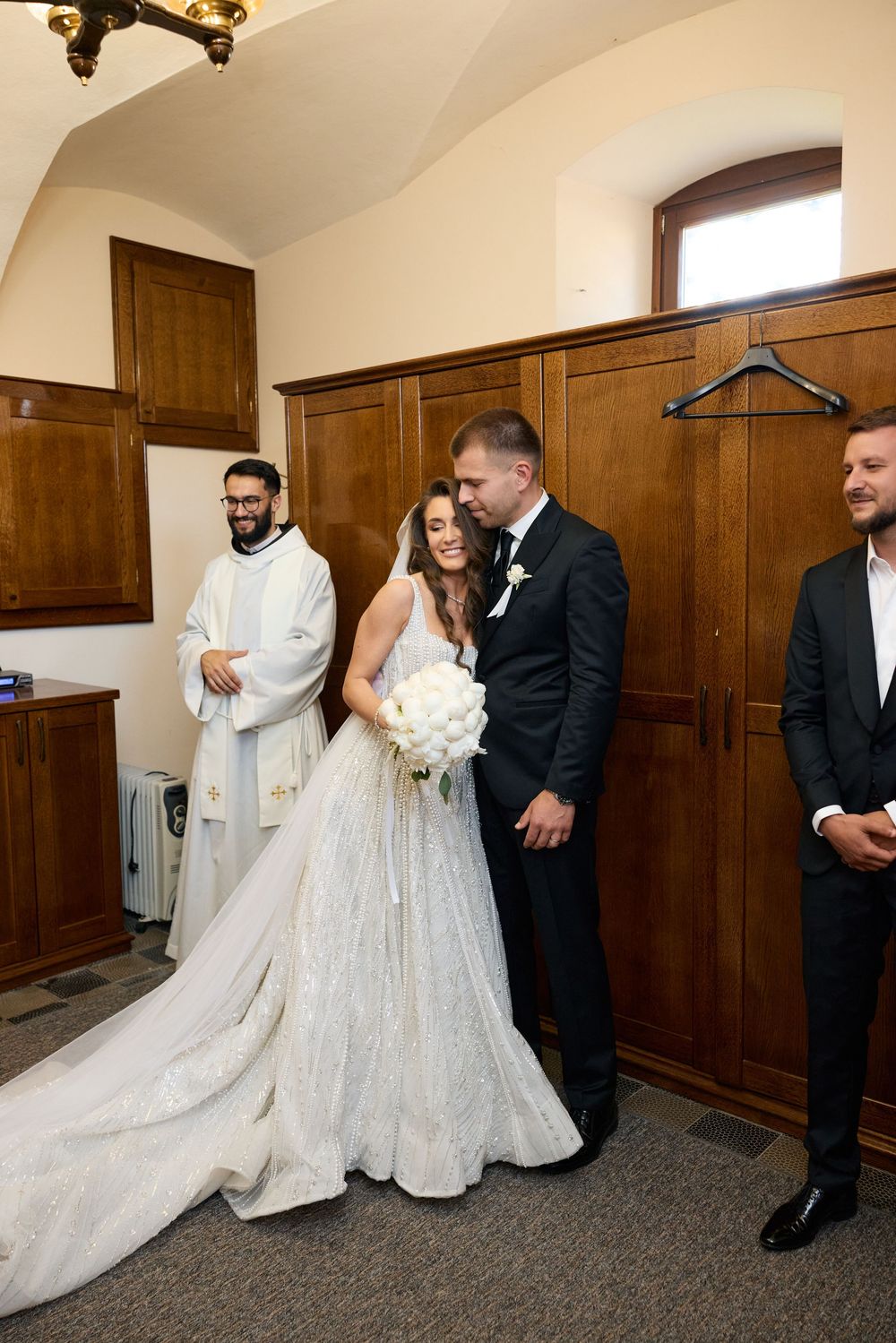 Bride and groom share intimate moment with officiant during wedding ceremony in wood-paneled room.