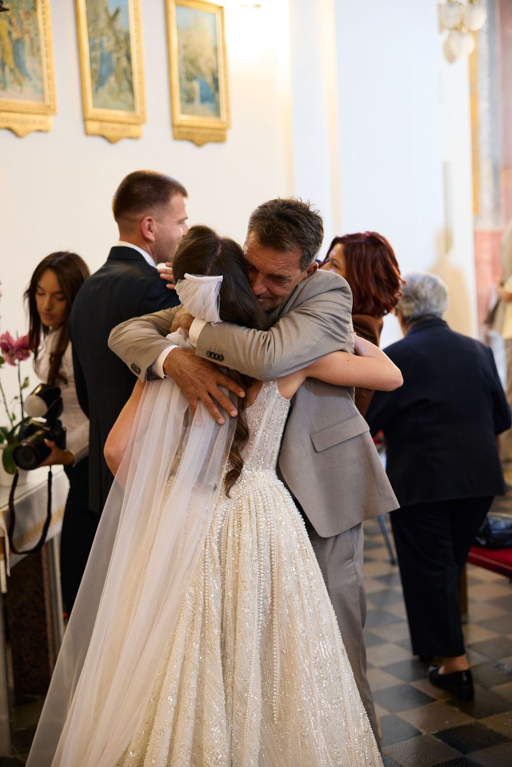 Bride in white gown embracing a guest during a wedding reception inside a decorated church.