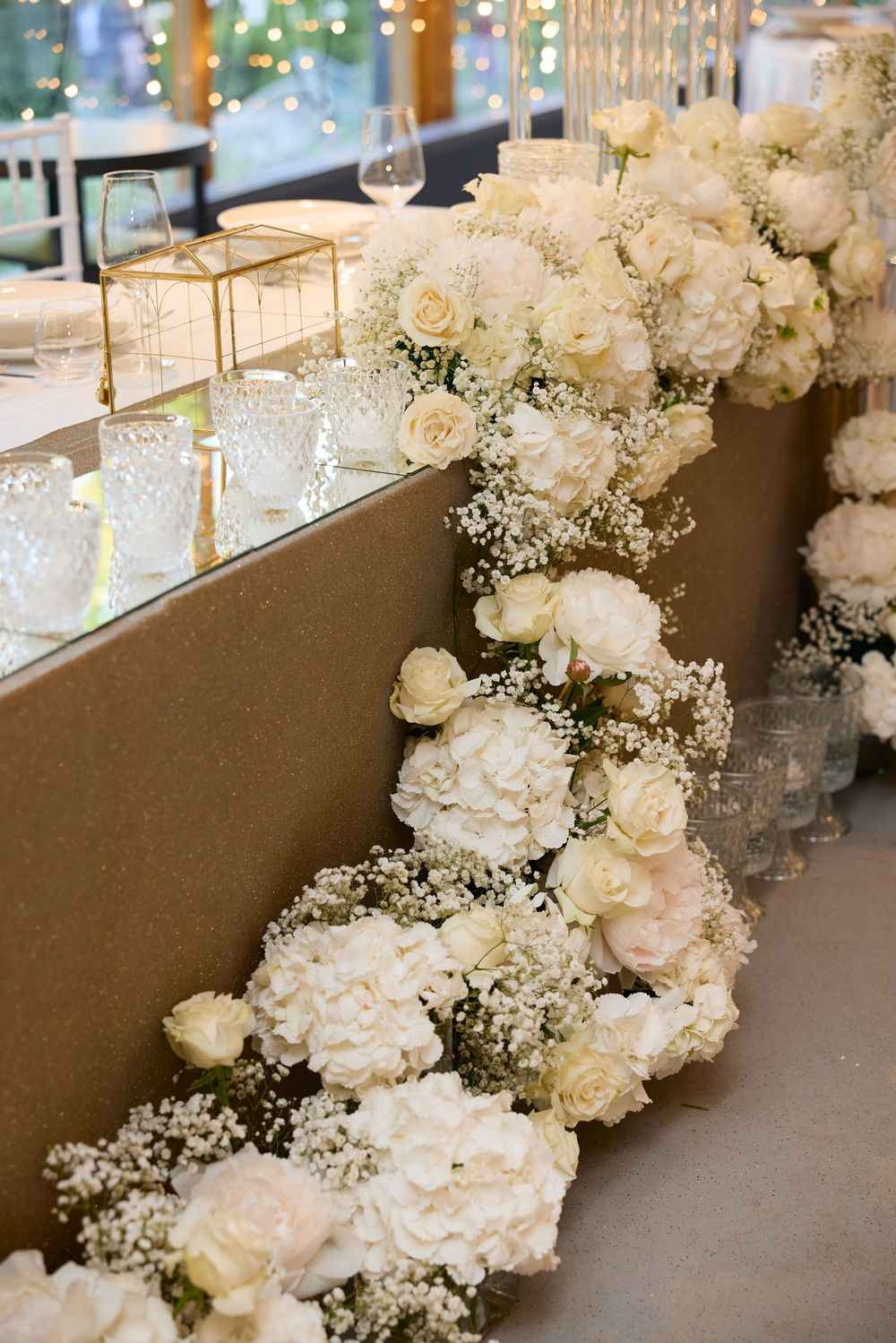 Elegant white floral table runner with roses and baby's breath at wedding reception.