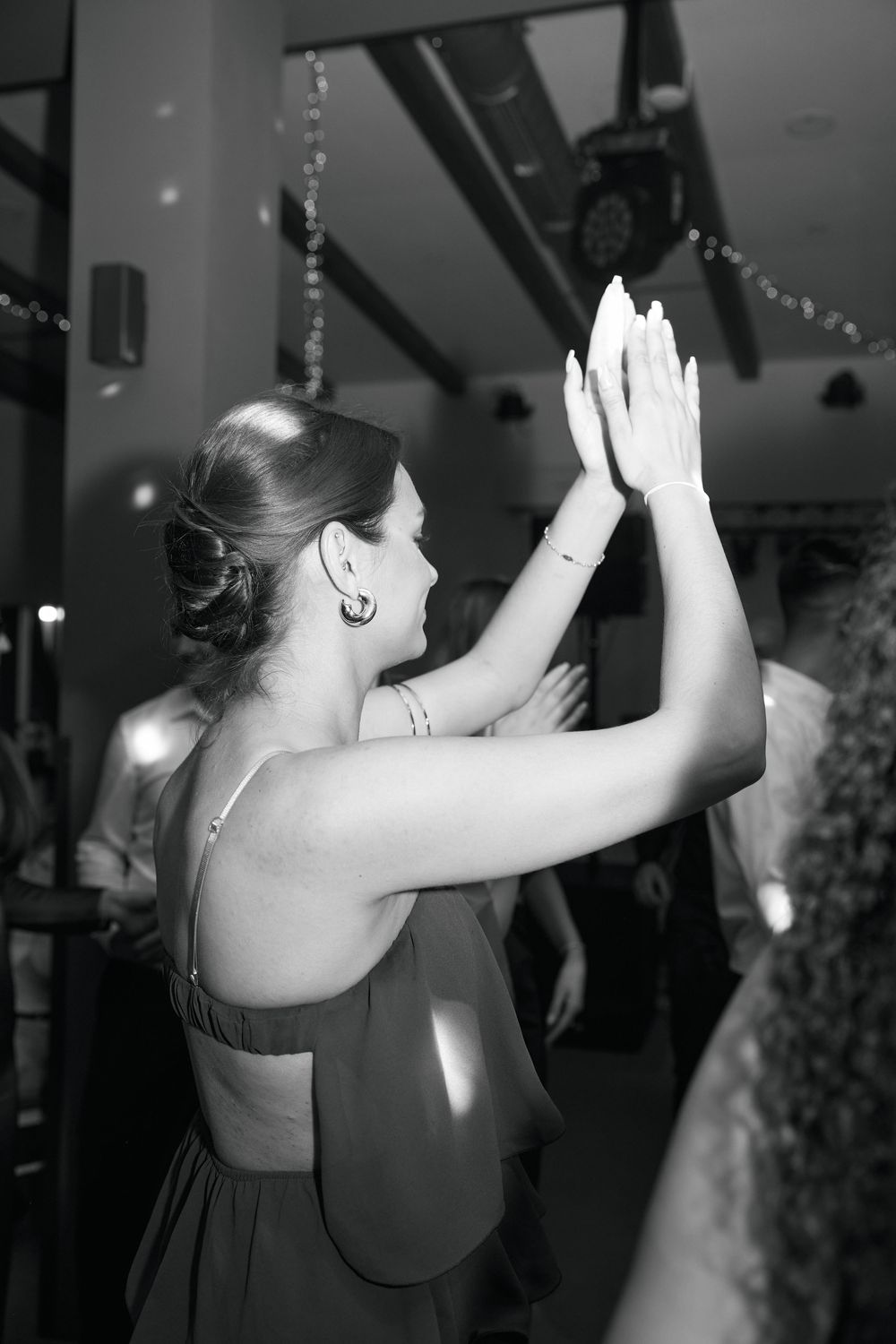 Black and white photo of a woman in a backless dress clapping her hands at a wedding reception dance floor.