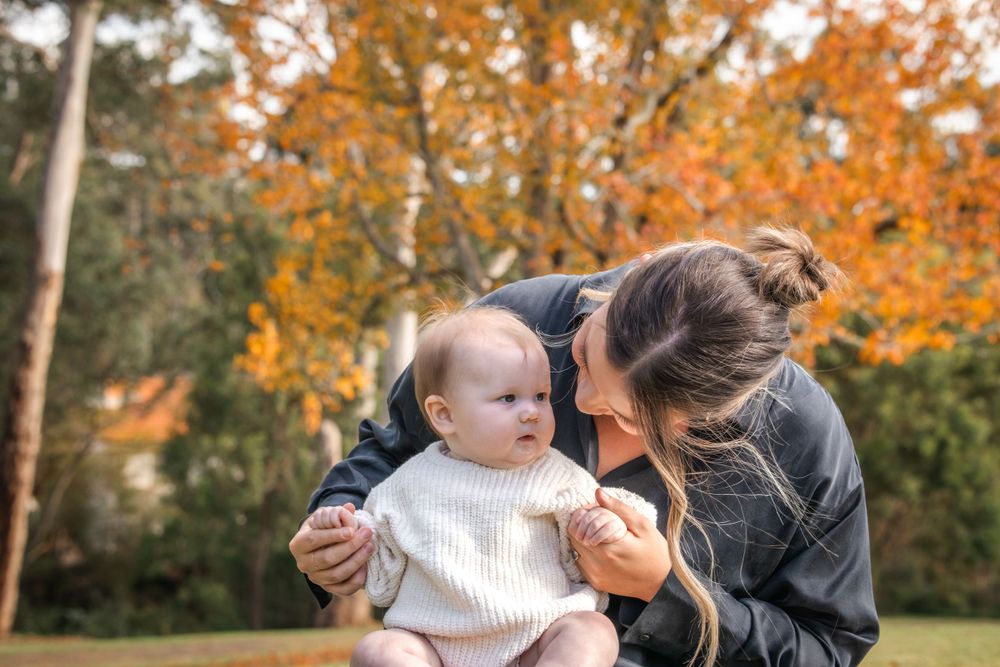 Parent and baby share a tender moment together on an autumn day surrounded by golden fall foliage at Castle Hill Heritage Park.