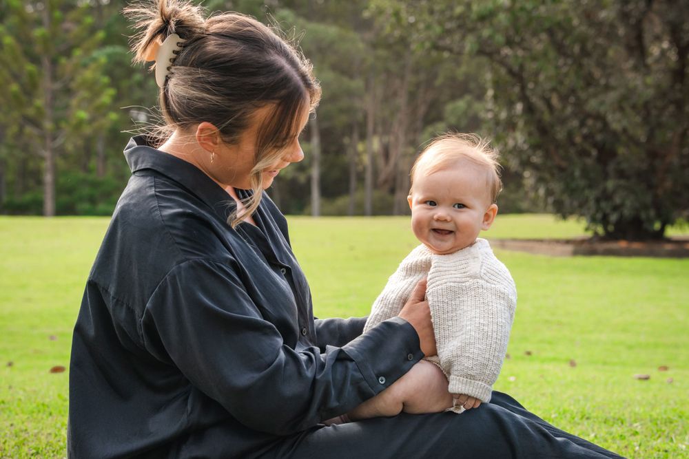 A joyful outdoor moment shared between a baby wearing a cream sweater and their caregiver at Castle Hill Heritage Park.
