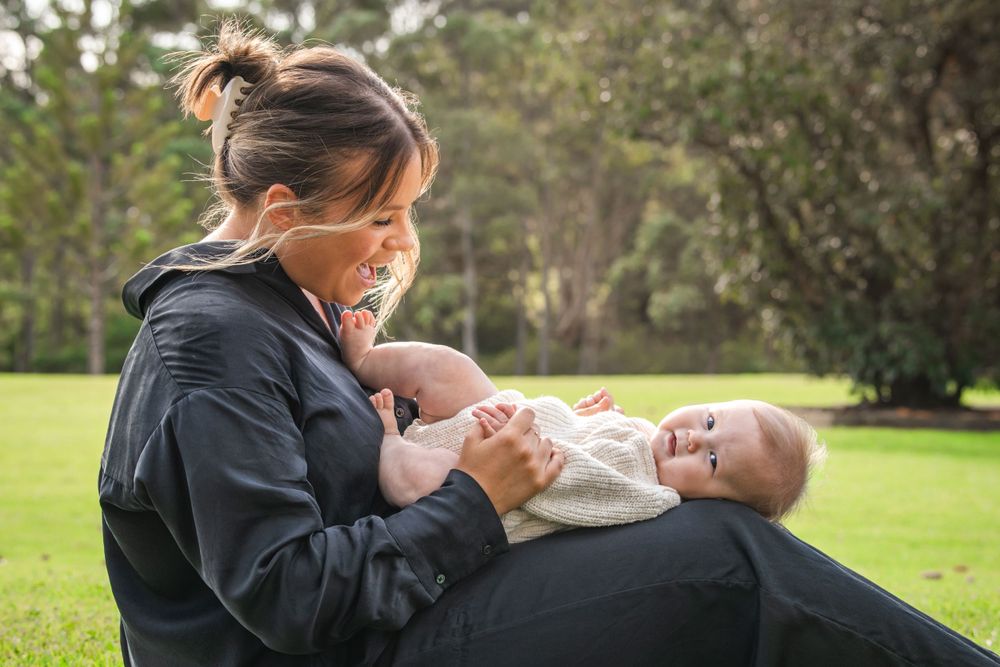 Someone in a navy hoodie comforting a small baby while sitting on grass in a peaceful outdoor setting.