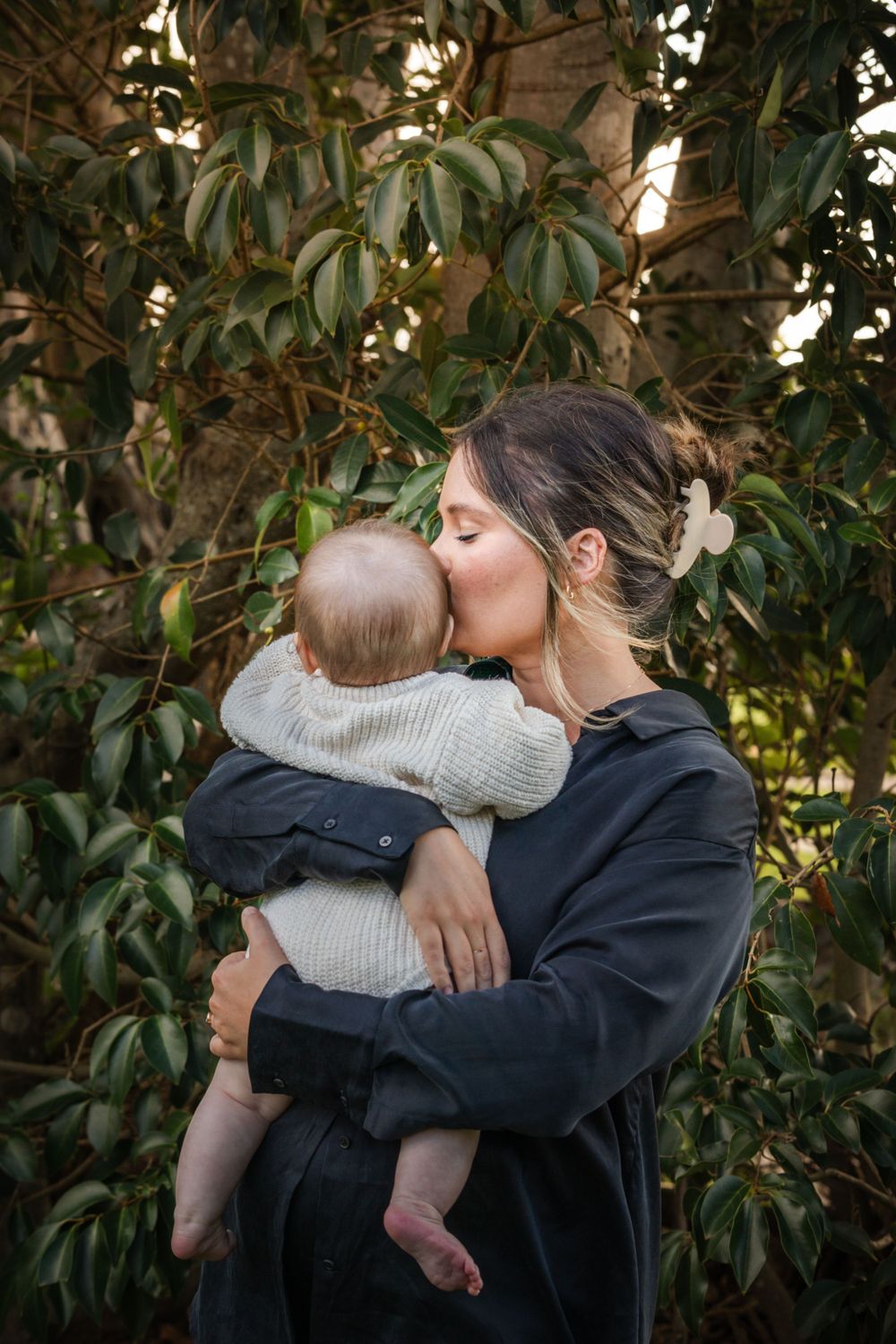 A touching embrace between parent and child amidst lush green foliage in natural lighting at Castle Hill Heritage Park.