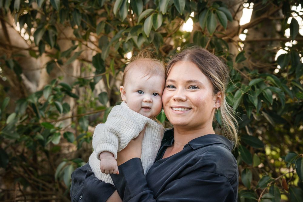 A heartwarming portrait outdoors with a smiling woman in black holding a contented baby in a cream sweater.