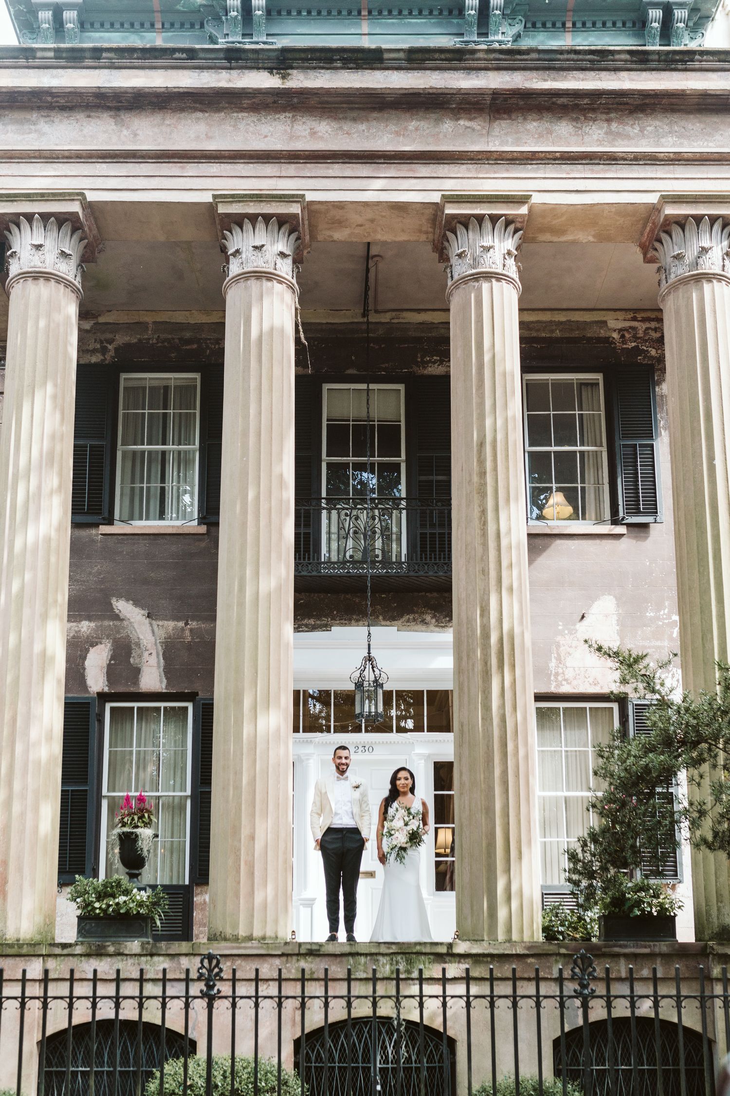 Bride and groom posing between grand columns of historic building entrance on their wedding day.