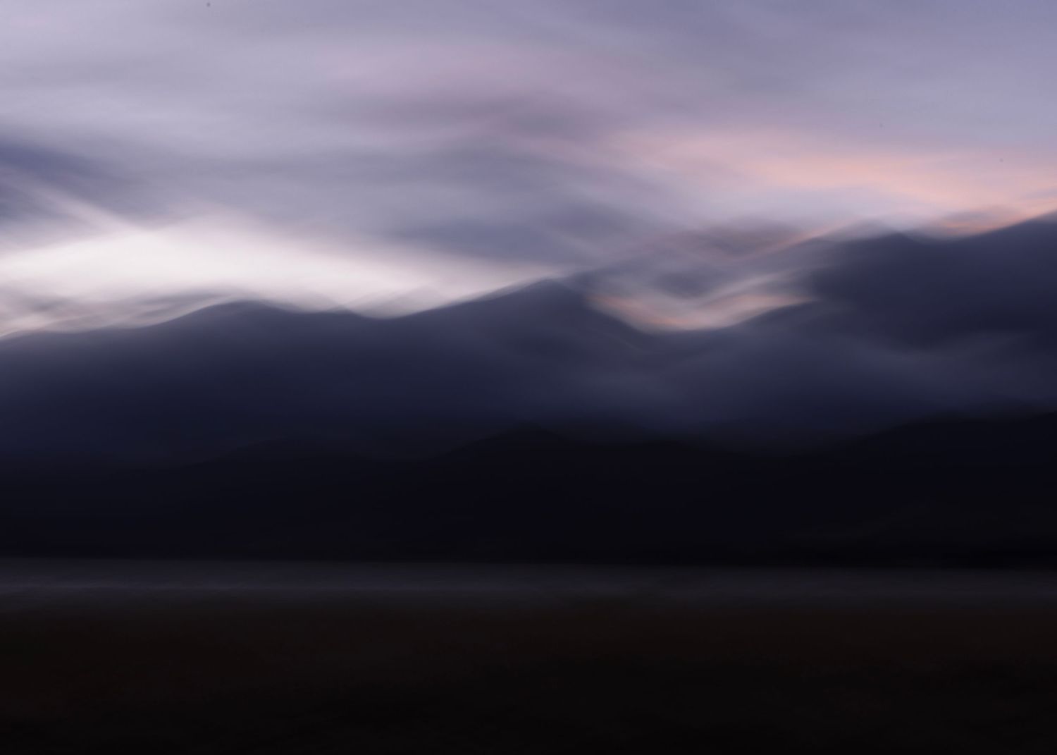 Dramatic dark mountain landscape at dusk with swirling clouds in purple and pink hues over shadowy peaks.