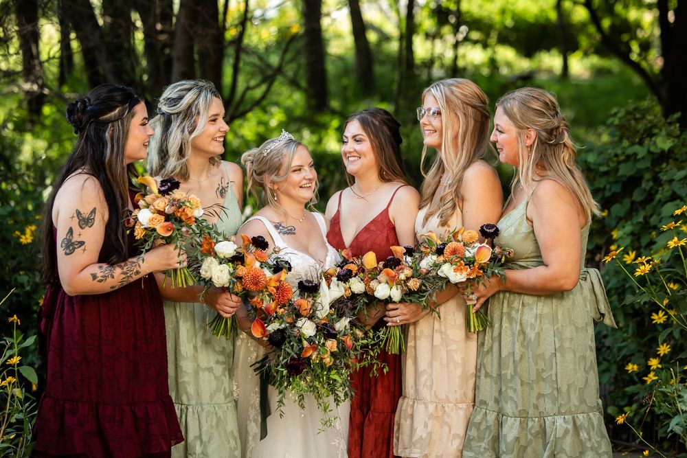 Bride and bridesmaids in mismatched green and red dresses holding lush floral bouquets outdoors in a garden setting.