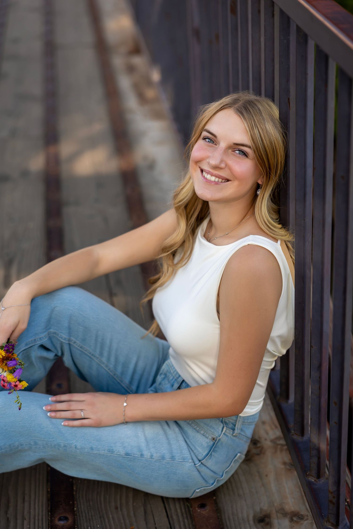 Portrait of girl sitting on bridge smiling wearing jeans and a white top