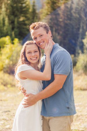 Happy couple hugging and smiling together in a scenic mountain meadow with pine trees on a bright sunny day.