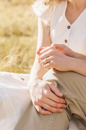 Close-up of couple holding hands outdoors in sunny field, woman wearing elegant ring on finger.