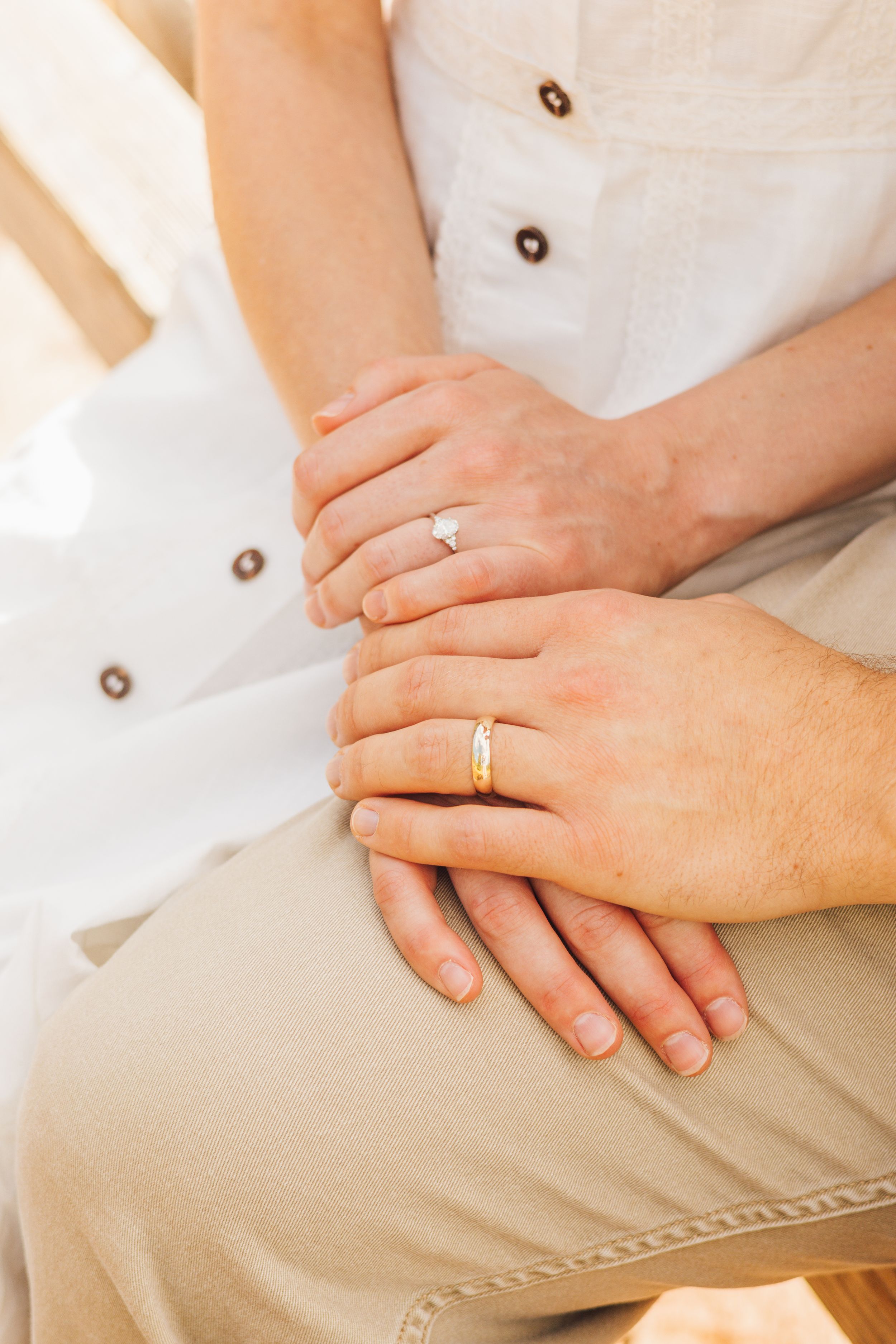 Couple holding hands showing engagement ring and wedding band while sitting together outdoors.
