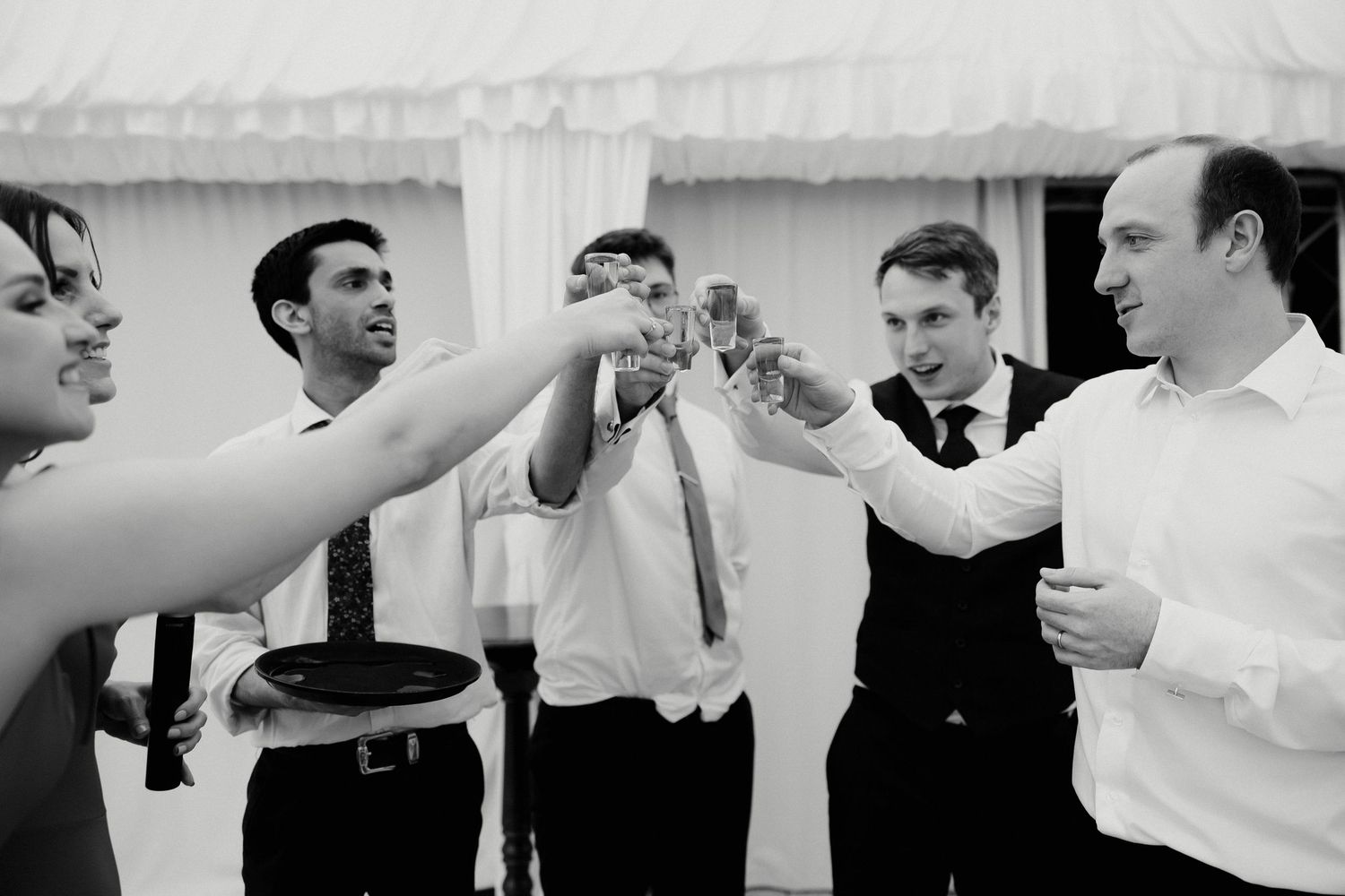 Black and white photo of wedding guests clinking glasses in a celebratory toast at a reception.