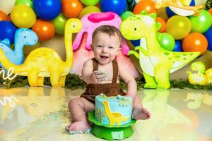 Baby smiling at first birthday dinosaur cake smash with colorful balloon backdrop and cute dino decorations.