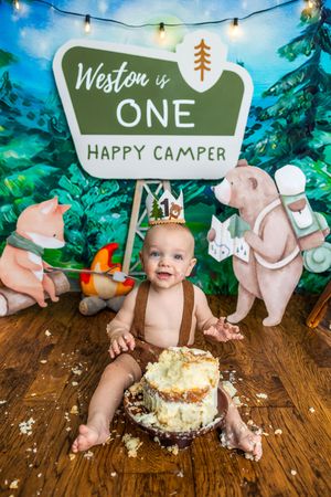Baby Weston celebrates his first birthday with a cake smash at a camping-themed party with a Happy Camper sign.