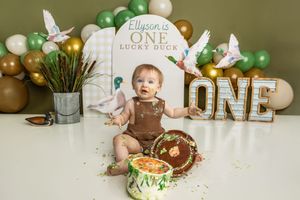 Baby's first birthday cake smash with duck theme, green balloons, and ONE marquee letters on green background.