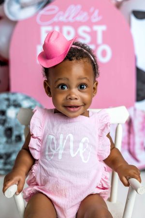 Adorable baby girl in pink cowboy hat and 'one' romper celebrating her first rodeo birthday party.