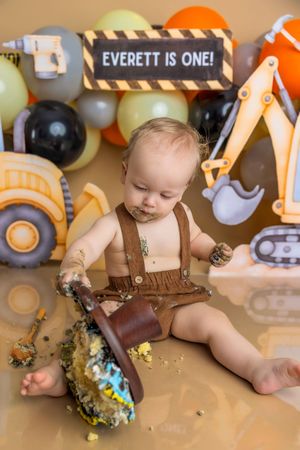 Baby Everett celebrates his first birthday with a construction-themed cake smash, surrounded by trucks and balloons.