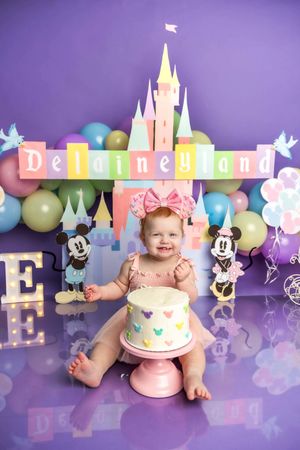 Baby girl celebrates first birthday with Disney-themed cake smash featuring Minnie Mouse decor and colorful balloons.