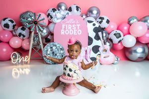 Baby girl celebrates her first birthday with a cowgirl rodeo cake smash surrounded by pink balloons and disco decor.