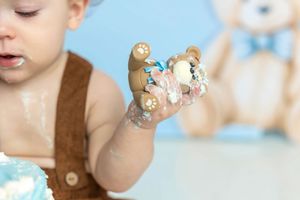 Baby holding a frosted teddy bear figurine with cake smash during first birthday photo session.