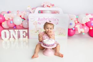 Adorable baby girl tastes first birthday cake at Aubriella's pink ONE themed cake smash photo shoot.