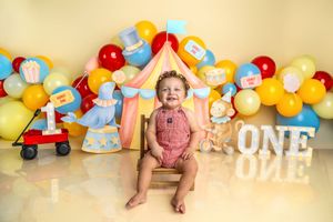 Baby smiling at first birthday circus themed photo shoot with colorful balloons and ONE sign.