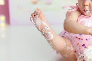 Close-up of baby's foot covered in white birthday cake frosting during first birthday cake smash.