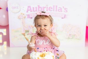 Baby girl in pink dress enjoys her first birthday cake smash at Aubriella's ONE themed party with giraffe decor.