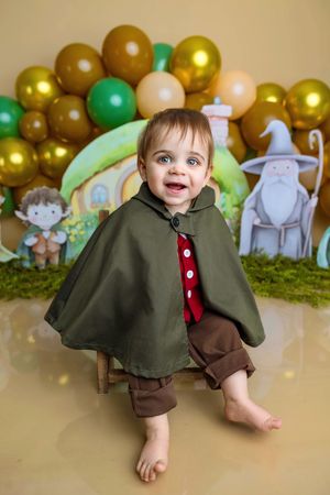 Adorable baby in Hobbit costume with green cape and red tie at a Lord of the Rings themed first birthday party.