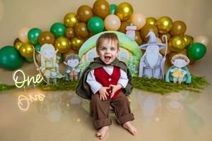 Smiling baby at Lord of the Rings themed first birthday party with green balloons and fantasy character cutouts.