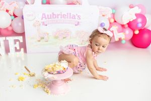 Baby girl crawls toward smashed pink birthday cake at Aubriella's first birthday cake smash session.