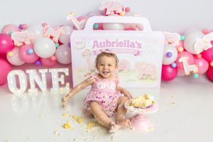 Baby girl in pink romper celebrates first birthday smashing cake at Aubriella's ONE themed photo shoot.