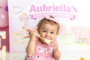 Baby girl in pink outfit eating cake at her first birthday party smash cake photo session.