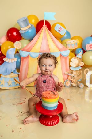 Baby's first birthday cake smash with circus theme, colorful balloons, and rainbow cake.