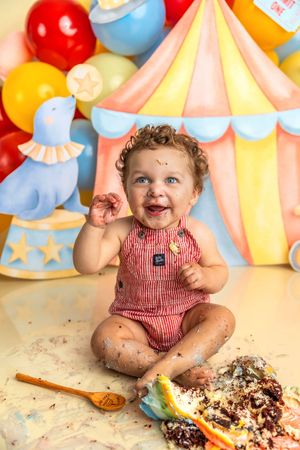 Happy baby covered in cake at colorful circus-themed first birthday cake smash photo shoot.